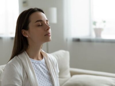Calm serene woman resting sitting on couch in modern living room closed her eyes breath fresh humidified air. Fatigue relief repose, boost inner balance and mindfulness, meditation practice concept