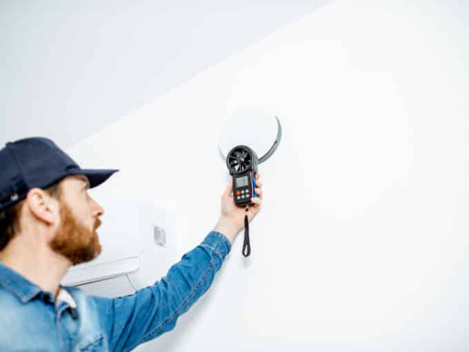 Handyman checking the speed of air ventilation with measuring tool on the white wall background