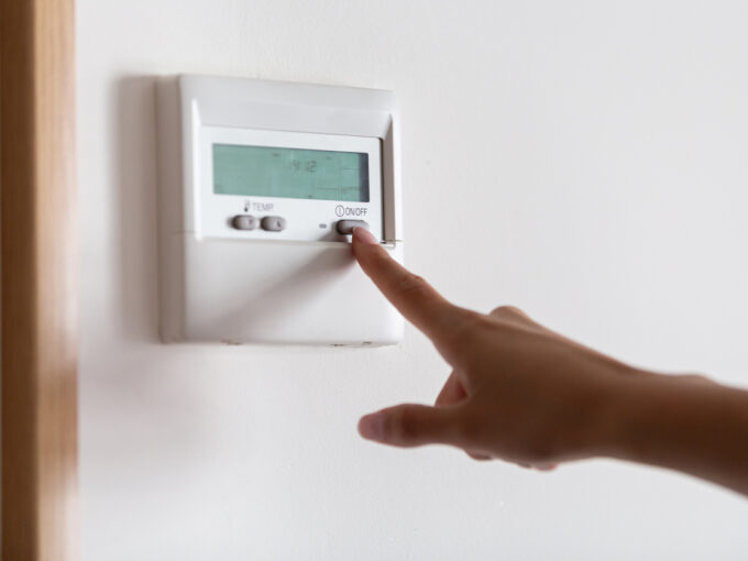 Close-up of a young woman's hand pressing the on/off button of the air conditioner or heater